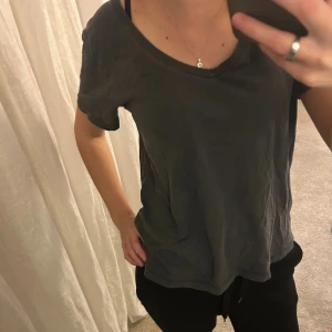 Mörkgrå t-shirt med v-ringning - Snygg mörkgrå t-shirt med v-ringad hals och korta ärmar. Modellen är loose fit och har en enkel, stilren design utan mönster eller detaljer. Perfekt för dig som gillar en avslappnad och cool look. Materialet känns mjukt och skönt mot huden.