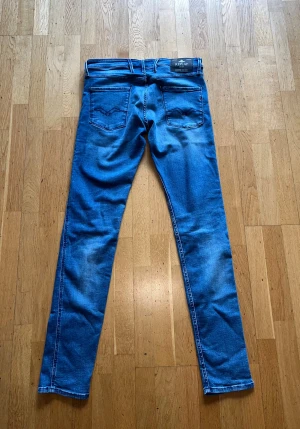 Replay Anbass blå jeans slim fit - Snygga Replay Anbass jeans i klassisk blå färg med slim fit och raka ben. Jeansen är aldrig använda. Jeansen har fem fickor, dragkedja och knappstängning. Materialet är stretchigt jeans för skön passform. Perfekt för dig som gillar stilrena och moderna jeans.