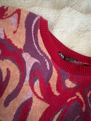 Färgstark mönstrad tröja från Zara - Säljer en unik och färgstark tröja från Zara med swirl-mönster i rött, lila och beige. Tröjan har rund hals med ribbad kant och långa ärmar. Perfekt för dig som vill sticka ut med coola färger och mönster. Storleken är lite fel det står att det är en L men den sitter som en S
