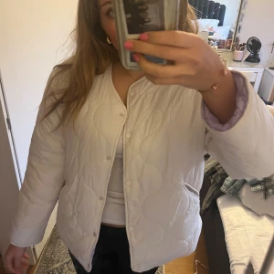 Vit quiltad jacka med lila foder - Quiltad vit jacka i storlek S. Den är lila på insidan så om man vill kan man vända den då den går att ha på båda hållen. Prislappen kvar.