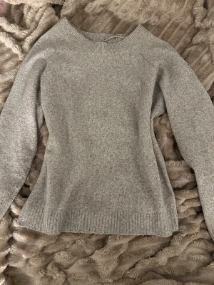 Grå stickad tröja med rund hals - Mysig beige/brun stickad tröja med rundad hals och ribbade muddar vid ärmslut och nederkant. Perfekt för kyliga dagar och enkel att matcha med jeans eller kjol. Långärmad och har en klassisk, stilren look som funkar till många olika outfits.