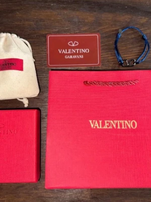 Blått Armband - Snyggt blått V armband med justerbart band i textil och en metallfärgad V-logga i mitten. Kommer med originalförpackning och tygpåse. Perfekt accessoar för dig som gillar exklusiva detaljer och stilren design, perfekt för att lyfta upp dina outfits. Mycket bra skick, bara använd ett fåtal gånger. Dm:a mig för fler frågor :)