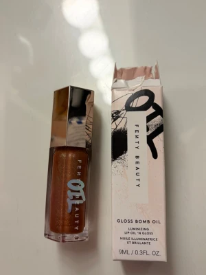 Fenty Beauty Gloss Bomb Oil läppglans - Fenty Beauty Gloss Bomb Oil är ett läppglans i en snygg brun nyans med skimrande finish. Kommer i en stilren fyrkantig förpackning med silvrigt lock. Oljebaserad formula som ger glans och återfuktning till läpparna. Innehåller 9 ml. Helt ny!!