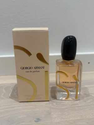 Giorgio Armani Sì Eau de Parfum 50ml - Giorgio Armani Sì Eau de Parfum i elegant glasflaska med svart kork och guldiga detaljer. Doften kommer i en stilren beige kartong med stora guldfärgade bokstäver. Flaskan rymmer 50 ml och har en exklusiv och modern design som känns lyxig. HELT NY