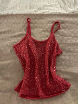Rosa paljettlinne med smala axelband - Säljer ett rosa linne med smala axelband och glittriga paljetter över hela tyget. Toppen har en lätt figursydd passform och är perfekt för dig som gillar att sticka ut. Materialet är mjukt och stretchigt för en bekväm känsla.
