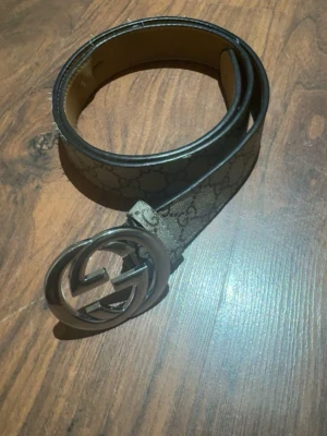 Gucci beige bälte med GG-spänne - Snyggt beige bälte från Gucci med klassiskt GG-mönster och stort metallspänne med dubbla G. Perfekt accessoar för att lyfta din outfit med en lyxig touch. Bältet har en stilren design och är tillverkat i skinn med detaljer i metall.