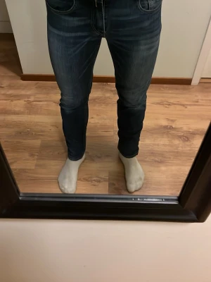 Mörkblå slim fit jeans från Replay - Säljer ett par mörkblå slim fit jeans från Replay med snygga slitningar och klassiska fem fickor. Jeansen har en något tvättad look och sitter tight över benen. Perfekta för dig som gillar en modern och stilren stil.