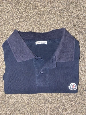 Mörkblå Moncler piké - Mörkblå pikétröja från Moncler. Storlek S. Använd ett flertal gånger, enda defekten är att siffrorna på etiketten är något svårlästa. 8/10 skick