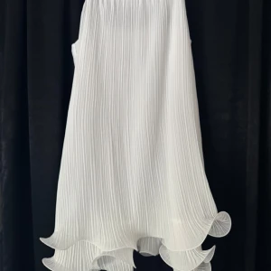 Vit plisserad klänning med volangkant - Supersnygg vit klänning med plisserat tyg och vågig volangkant längst ner. Klänningen har en luftig känsla och är perfekt för sommarens tillfällen. Aldrig använd och prislapp kvar