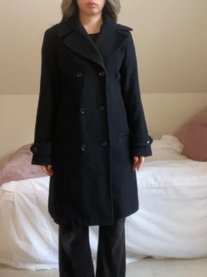 Svart dubbelknäppt kappa - Jätte fin svart dubbelknäppt kappa från Mango. Perfekt till en formell outfit men även till vardags. Står storlek UK: M, USA: S. Jag skulle säga att den passar flera olika storlekar xs-m. Jag på bilden är xxs-s. 