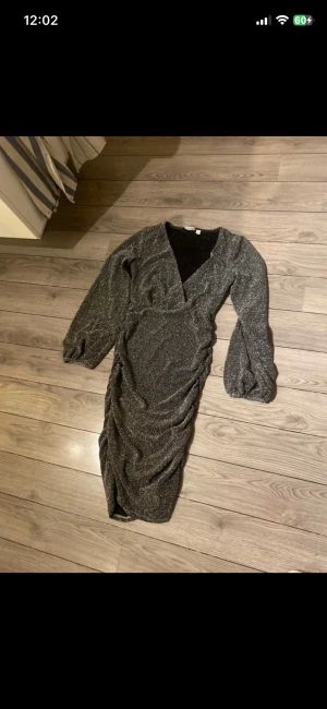 Glittrig silver klänning med v-ringning - Snygg glittrig silverfärgad klänning med v-ringning och långa puffärmar. Klänningen har en åtsittande passform med rynkade detaljer längs sidorna och slits nedtill. Perfekt för dig som vill sticka ut med en festlig look.   Finns några trådar som sticker ut när man synar klänningen se sista bild   Är storlek xs men passar bättre en S 