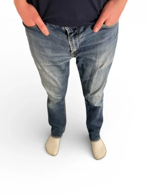 Blå Levi's raka jeans w 33 L 32 - Säljer ett par skit snygga klassiska blå Levi's jeans med rak passform och snyggt slitna detaljer. Jeansen har fem fickor, dragkedja och knappgylf samt den ikoniska läderlappen bak i midjan. Perfekta för en avslappnad och cool stil.