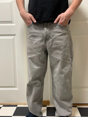 Baggy grå jeans med rak passform - Baggy grå jeans med rak passform och klassisk femficksdesign. Jeansen har en avslappnad look och är tillverkade i kraftigt denimtyg. Perfekta för en chill och trendig stil.