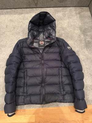 Colmar vinterjacka  - Snygg mörkblå dunjacka från Colmar med huva och dragkedja framtill. Jackan har två sidofickor med dragkedja och en logotyp på ärmen. Storlek small och i 9/10 skick, hör av dig vid minsta möjliga fundering ✅