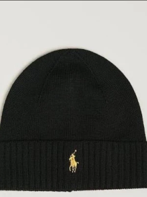 Svart mössa från Polo Ralph Lauren - Snygg svart stickad mössa från Polo Ralph Lauren med klassisk gul broderad logga framtill. Mössan har ribbad kant och är tillverkad i mjukt material som håller dig varm under kalla dagar. Perfekt accessoar för en stilren look.