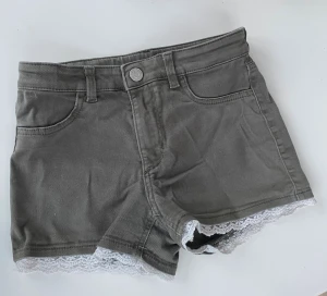 Gröna shorts med spetsdetalj - Snygga lågmidjade gröna shorts med vit spetskant längst ner. Klassisk femficksmodell med knapp och dragkedja framtill. Perfekta för sommaren och ger en söt touch till din outfit.