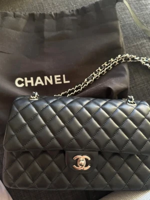 Chanel svart quiltad handväska - Säljer en klassisk svart quiltad handväska från Chanel med silverfärgad kedjerem och ikoniskt CC-spänne. Väskan är tillverkad i mjukt läder och har innerfack med dragkedja. Perfekt för dig som vill ha en tidlös och lyxig accessoar. Kvitto finns privat!