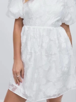 Vit kort klänning med puffärm - Supersöt vit kort klänning med puffärmar och blommigt mönster i tyget. Klänningen har öppen rygg med knyt och volangdetaljer som ger en romantisk vibe. Perfekt för student, konfirmation eller midsommar!❤️