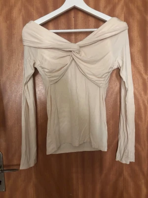 Beige offshoulder topp Gina Tricot - Trendig beige offshoulder topp från Gina Tricot med twistad detalj framtill. Långärmad och figurnära passform, perfekt för dig som vill ha en stilren men ändå unik look. Tillverkad i mjukt material som känns skönt mot huden. Super fin och inte använd nån gång