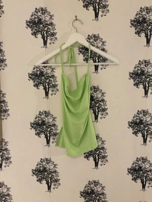 Ljusgrön halterneck linnetopp - Trendig ljusgrön linnetopp med halterneck och draperad front. Toppen har tunna axelband som knyts i nacken och en lös, flowy passform. Perfekt för varma dagar och somriga outfits.