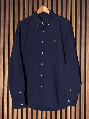 Mörkblå Ralph Lauren skjorta - Klassisk mörkblå skjorta från Ralph Lauren med slim fit-passform. L i storlek. Skick 10/10. Hör av er vid funderingar. Pris ej hugget i sten