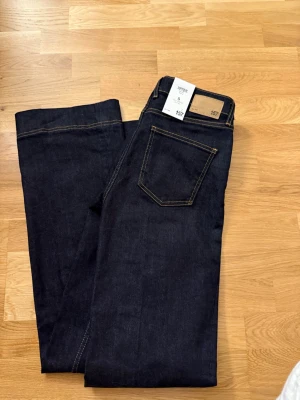 Mörkblå bootcut jeans från 157 - Säljer ett par mörkblå vida jeans från 157, modell Upper med mid rise och full längd. Jeansen har klassiska kontrastsömmar och femficksdesign. Perfekta för dig som gillar en tidlös och clean look. Med prislapp 