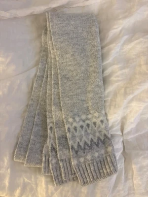 Ljusgrå halsduk från lager 157 med mönster - Mysig ljusgrå halsduk från lager 157 med diskret mönster i vitt och grått vid kanterna. Stickad i mjukt material som känns skönt mot huden. Perfekt för kalla dagar och enkel att matcha till olika outfits.
