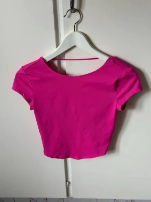 Rosa croppad topp med kort ärm - Snygg croppad topp i stark rosa färg med korta ärmar och bred, rundad urringning både fram och bak. Toppens material känns mjukt och stretchigt, perfekt för en trendig look. Passar dig som gillar färg och vill sticka ut.