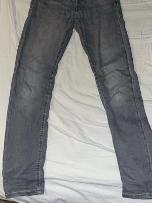 Grå raka jeans i klassisk modell jack & jones - Säljer ett par grå jeans med rak passform och klassiska fem fickor. Jeansen har en snygg tvättad look och är perfekta för en avslappnad stil. Materialet är denim och de har dragkedjegylf. Passar dig som gillar enkel och tidlös design.