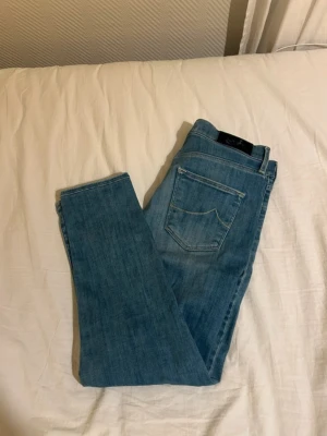 Ljusblå jeans från Jacob cohen - Säljer ett par ljusblå jeans med klassisk femficksdesign och gul kontrastsöm. Jeansen har en smal passform och är tillverkade i mjukt denimtyg som sitter snyggt. Perfekta till en avslappnad och trendig look. Passar bättre till W27 L27. Går inte ner i pris.