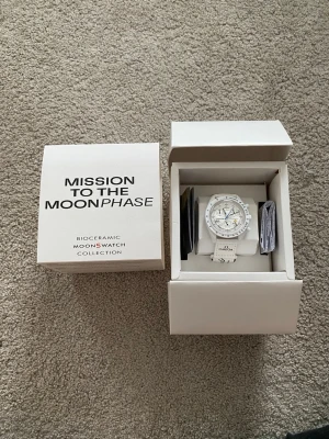 Omega x Swatch MoonSwatch Snoopy X Woodstock - Säljer en Omega x Swatch MoonSwatch Mission to the Moonphase i vit biokeramik. Klockan har vit urtavla med svarta detaljer, blå sekundvisare och Snoopy-motiv. Vit rem med Omega-logga. Levereras i originalförpackning.