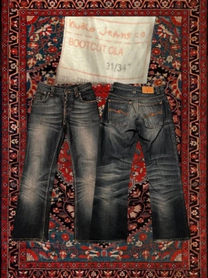 Nudie Jeans bootcut Ola  - Säljer ett par blå bootcut jeans från Nudie Jeans med slitningar och kontrastsömmar. Jeansen har klassisk femficksdesign, orange brodyr på bakfickorna och råa kanter vid bensluten. Perfekta för en avslappnad och trendig look. Obs mindre i storlek, be om mått om ni önskar 