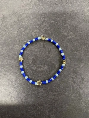 Blått pärlarmband med stjärnor Storlek M  - Ett armband med små blå och ljusblå pärlor samt guldiga stjärnformade pärlor. 