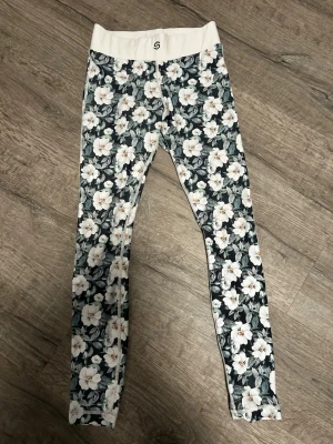 Blommiga leggings med hög midja från stranger - leggings med blommigt mönster i vitt och grönt. Hög midja med bred vit linning och tight passform. 