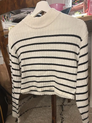 Vit stickad tröja med svarta ränder H&M. Funkar om man är xs och man vill ha en tröja som nästa är magtröja. - Vit ribbstickad tröja från H&M med svarta horisontella ränder. Tröjan har hög hals och långa ärmar, samt en något croppad passform. Perfekt för en avslappnad och trendig look. Materialet är mjukt och bekvämt.