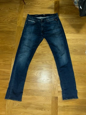 Replay Grover blå jeans straight fit - Snygga blå Replay Grover jeans i straight fit med klassisk femficksdesign och diskreta slitningar. Jeansen har normal passform och är tillverkade i slitstarkt bomullsdenim. Midjan 33 och längd 32 och passar en person mellan 170-180 cm.