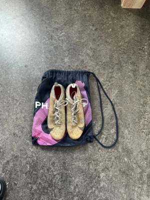 Nike Vapor Mercurial  - Säljer ett par Nike Mercurial fotbollsskor i gul och svart med vita skosnören. Skorna har en låg profil och är tillverkade i syntetmaterial för bra grepp och känsla på planen. Sulan är röd undertill och skon har klassisk Nike-logga på sidan. Perfekta för dig som vill ha speed på planen.