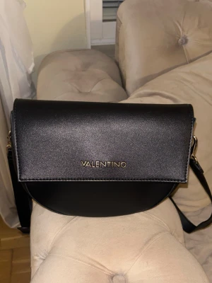Valentino Väska - Säljer en Valentino by Mario Valentino crossbody-väska. Aldrig använd – fick den i present men den är tyvärr inte min stil. Svart med gulddetaljer, i nyskick. 