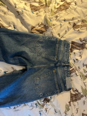 Blå mom jeans med hög midja - Säljer ett par klassiska blå mom jeans i denim med hög midja och raka ben. Jeansen har två stora bakfickor och en tidlös tvätt. Perfekta för en avslappnad och trendig look.