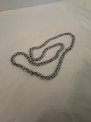 Silverfärgat kedjehalsband - Stilrent halsband i silverfärgad metall med breda, platta länkar. Kedjan har en klassisk design som passar till många olika stilar. Perfekt accessoar för att lyfta din outfit med en cool och modern touch.