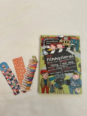Barnbok:  - En färgglad och illustrerad bok ur serien LasseMajas Detektivbyrå, 'Filmmysteriet', skriven av Martin Widmark och illustrerad av Helena Willis. Hårdpärm med tecknade figurer på omslaget. Tre bokmärken medföljer.
