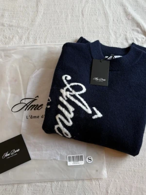Mörkblå mohairtröja från Âme Dorée - Mörkblå stickad mohairtröja från Âme Dorée med vit broderad text längs framsidan. Tröjan har rund halsringning och lång ärm, perfekt för höst och vinter. Materialet är mjukt och fluffigt mohair som ger en lyxig känsla.