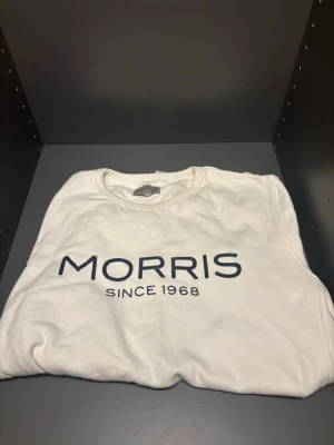 Vit sweatshirt från Morris - Vit sweatshirt från Morris med svart tryck 'MORRIS SINCE 1968' på bröstet. Klassisk rund halsringning och långa ärmar. Perfekt för en avslappnad och stilren look.