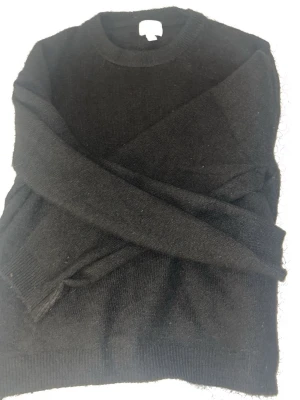 Svart stickad tröja i ullmix - Klassisk svart stickad tröja med rund hals och långa ärmar. Tröjan är gjord i mjuk ullmix som känns skön mot huden och har ribbade muddar vid ärmslut och nederkant. Perfekt basplagg för lager på lager och enkel att matcha.