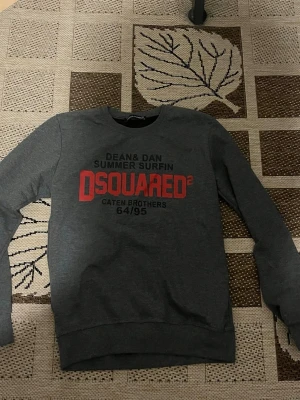 Grå sweatshirt från Dsquared2 - Snygg grå sweatshirt från Dsquared2 med tryck i rött och svart framtill. Rund halsringning och långa ärmar. Perfekt för en avslappnad och trendig look. Materialet känns mjukt och bekvämt mot huden. Storlek xs (170) 
