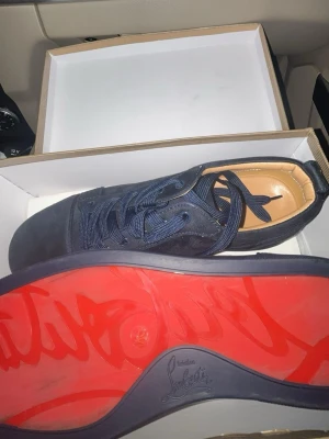 Marinblå Christian Louboutin sneakers - Snygga marinblå sneakers från Christian Louboutin med klassisk röd sula och diskret logga undertill. Skorna har ovandel i mocka och textil, rund tå och matchande marinblå snörning. Perfekta för dig som vill sticka ut med exklusiv stil. Ett till ett. Nästan helt nya!