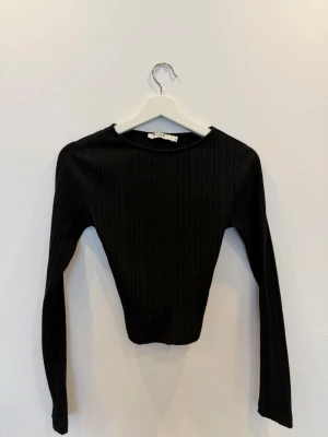 Svart ribbad långärmad topp NA-KD - Säljer en svart ribbad långärmad topp från NA-KD. Toppen har en rund halsringning och är tillverkad i ett stretchigt material som sitter snyggt på kroppen. Perfekt att styla med jeans eller kjol för en clean look.