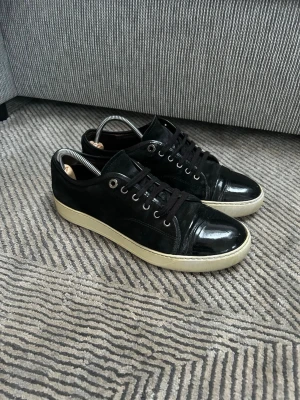Lanvin skor svarta  - Snygga svarta lanvin sneakers med både mocka och lackdetaljer. Skorna har svarta snören, metallfärgade öljetter och en vit sula som ger en clean kontrast. Perfekta för dig som gillar en stilren men ändå edgy look.