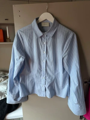 Blå randig skjorta från Neo Noir - Klassisk blå skjorta från Neo Noir med vita tunna ränder. Skjortan har lång ärm, breda manschetter och knappar framtill. Tillverkad i mjuk bomull och har en rak, något loose passform. Perfekt för en clean och stilren look.