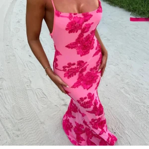 Klänning - Säljer en superfin rosa långklänning med stora blommiga mönster i starkare rosa. Klänningen har smala axelband med knyt och en figurnära passform som framhäver siluetten (axelbanden går också att reglera). Perfekt för sommarkvällar och speciella tillfällen. Materialet känns mjukt och följsamt. 🌸💗